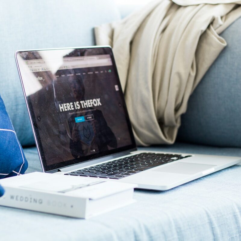 A laptop sitting next to a book on a couch.