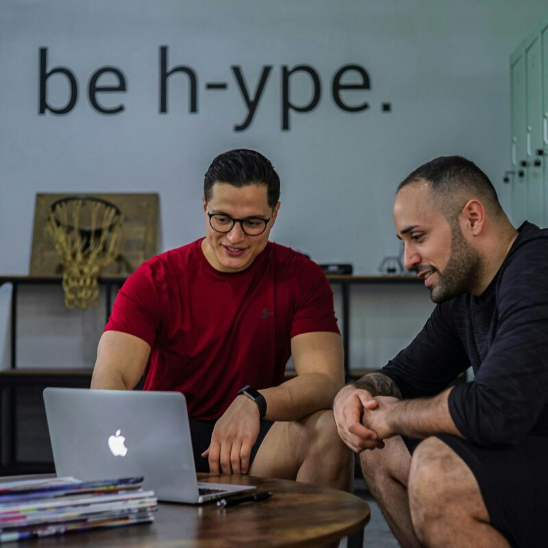 Two men sitting on a coffee table looking at a laptop