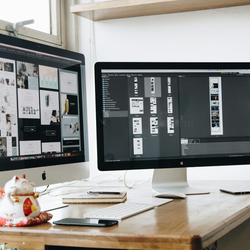 two computer monitors sitting on top of a wooden desk
